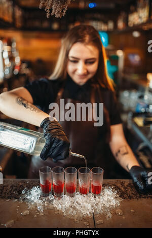 Weibliche Barkeeper in Handschuhe gießt Trinken in ein Glas. Frau Barkeeper mixen an der Theke im Pub. Barkeeper Besetzung Stockfoto