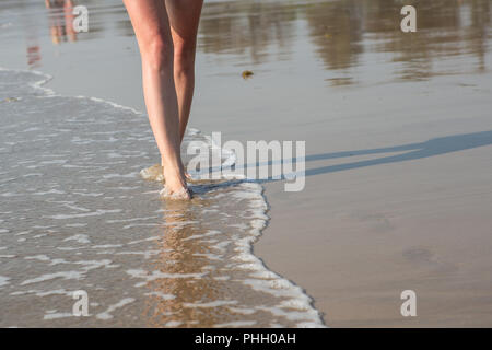 Eine Frau, die zu Fuß am Strand entlang an einem sonnigen Tag Stockfoto