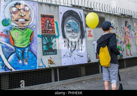 01.09.2018, Berlin: ein Junge fährt mit seinem Roller Vergangenheit der Deutschen Oper an der Fassade des Parkhauses, wo Werke der Kunst stecken geblieben sind. Es ist Teil der 'Einfügen - oben - Festival 2018". Es Künstler aus aller Welt zeigen ihre Kunst der Verklebung. Foto: Paul Zinken/dpa Stockfoto