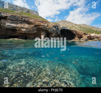 Große Höhle auf Küste mit Felsen und Schwarm von Fischen unter Wasser, geteilte Ansicht oberhalb und unterhalb der Wasseroberfläche, Mittelmeer, Costa Blanca, Spanien Stockfoto