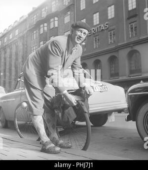 1950er Mann mit seinem Fahrrad. Ein Mann parkt sein Fahrrad und balanciert es auf dem Bordstein. Er legt eine Kette um das Hinterrad und verhindert, dass es gestohlen wird. Beachten Sie das Registrierungszeichen auf dem Fahrrad, das zu diesem Zeitpunkt obligatorisch war. Schweden 1954. Foto Kristoffersson Ref. BP57-5 Stockfoto