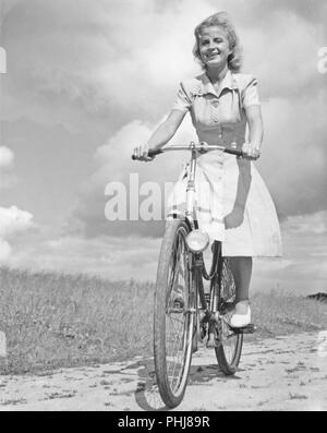 1940 Frau auf einem Fahrrad. Eine lächelnde junge Frau auf einem Fahrrad Frauen an einem sonnigen Tag. Schweden 1946 Stockfoto