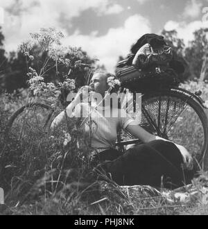 1940 Frau auf einem Fahrrad. Eine junge Frau hat ihr Fahrrad genommen und sich erholend auf einer Wiese. Schweden 1946 Stockfoto