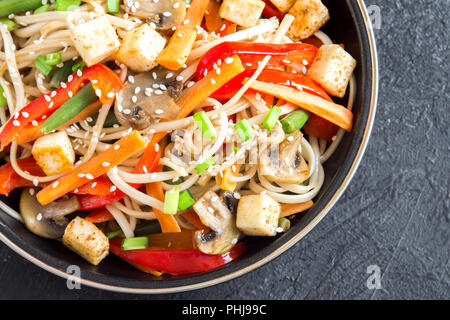 Pfannengerichte mit Udon-nudeln, Tofu, Pilzen und Gemüse. Asiatische vegan vegetarisch essen, Mahlzeit, Braten im Wok rühren über schwarzen Hintergrund, kopieren. Stockfoto