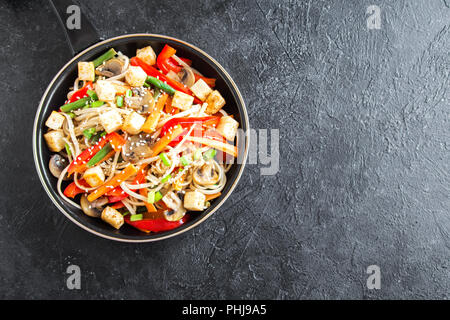 Pfannengerichte mit Udon-nudeln, Tofu, Pilzen und Gemüse. Asiatische vegan vegetarisch essen, Mahlzeit, Braten im Wok rühren über schwarzen Hintergrund, kopieren. Stockfoto