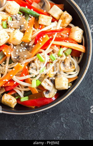 Pfannengerichte mit Udon-nudeln, Tofu, Pilzen und Gemüse. Asiatische vegan vegetarisch essen, Mahlzeit, Braten im Wok rühren über schwarzen Hintergrund, kopieren. Stockfoto