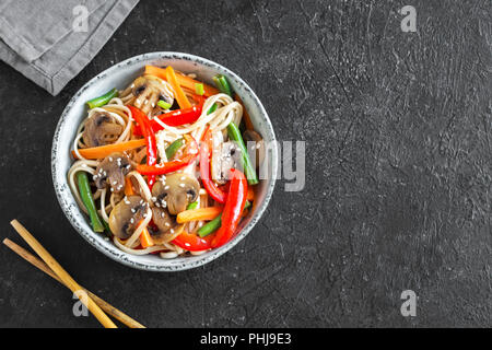 Pfannengerichte mit udon Nudeln, Pilzen und Gemüse in der Schüssel. Asiatische vegan vegetarisch essen, Mahlzeit, Bundesrepublik Jugoslawien über schwarzen Hintergrund rühren, kopieren. Stockfoto