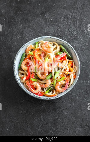 Pfannengerichte mit Udon-nudeln, Shrimps (Garnelen) und Gemüse. Asiatische gesundes Essen, Mahlzeit, Braten in der Schüssel verrühren über schwarzen Hintergrund, kopieren. Stockfoto