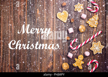 Frohe Weihnachten. Weihnachten Zuckerstangen, Lebkuchen in verschiedenen Formen, Haselnüsse, Walnüsse auf einem braunen Holztisch Stockfoto