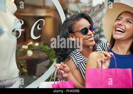 Nahaufnahme der lächelnden afrikanische Frau mit Lachen kaukasischen Freund während Einkaufstaschen draußen halten in der Nähe von Retail Store Fenster Stockfoto