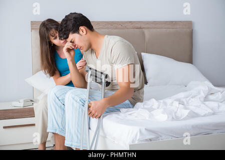 Junge Frau, die mann auf Krücken nach Verletzungen Stockfoto