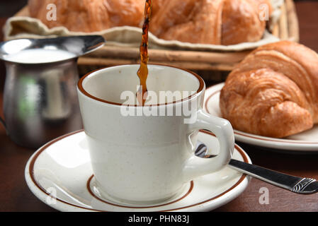 Kaffee ist in eine Schale mit Croissants im Hintergrund gegossen Stockfoto