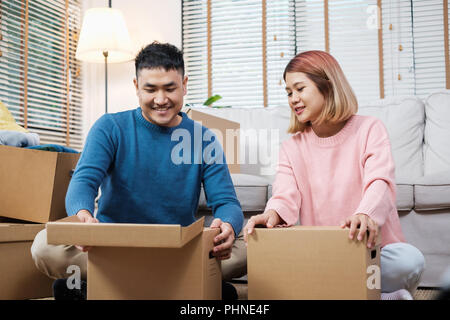 Gerne asiatische Paar offene Kartons während zum neuen Haus bewegen sich auf einem Sofa im Wohnzimmer. Auspacken für neues Haus Stockfoto