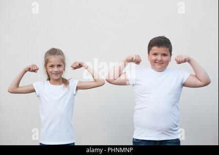 Zwei Kinder wenig dünnes Mädchen und dicken Jungen ihre Muskeln auf Copyspace Hintergrund Stockfoto