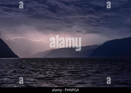 Tolle Aussicht mit einem Blitz, der in dunklen blauen Wolken bei einem Gewitter über einem See in den Bergen Stockfoto