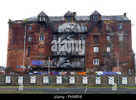 Eine riesige Brachflächen, leer und verlassen, rotes Backsteingebäude befindet sich auf Abfälle Boden und wird in interessanten Graffiti und Street Art in Glasgow, Schottland. Stockfoto