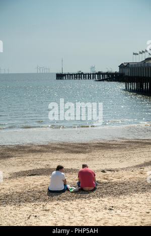 Clacton-on-Sea, Großbritannien. Übergewichtiger, übergewichtiger Mann und Frau sitzen am Clacton Beach in der Nähe von Groyne 41 Stockfoto