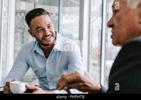 Junger Geschäftsmann, der mit einem Senior-Mann bei einer Tasse Kaffee spricht. Geschäftsleute, die sich während der Kaffeepause zwanglos unterhalten. Stockfoto