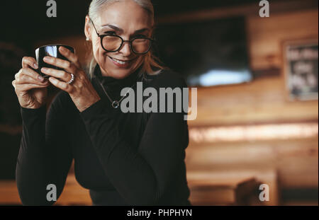 Portrait von älteren weiblichen tragen Brillen Kaffee trinken und Kamera. Gerne reife Lady mit einer Tasse Kaffee im Café. Stockfoto