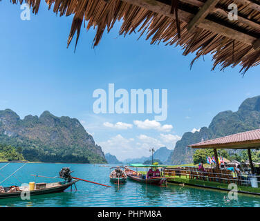 Holz- traditionelle thailändische Long-tail-Boot auf einem See mit Berge und Regenwald im Hintergrund an einem sonnigen Tag an Ratchaprapha Staudamm im Khao Sok Nationalpark, Thailand Stockfoto