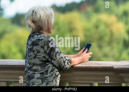 Frau lehnte sich auf einem Stein Attika halten ihr Handy in die Ferne starrt, als sie etwas Uhren Stockfoto