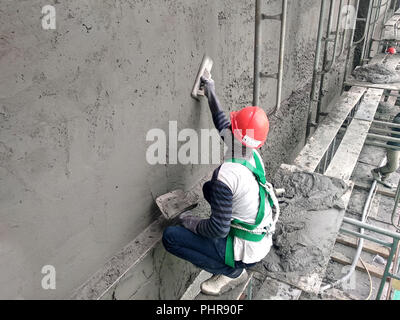 Bauarbeiter verputzarbeiten Wand mit Zementputz auf der Baustelle. Sie sind das Tragen geeigneter Schutzausrüstung, um zu verhindern, dass Schlimmes passieren. Stockfoto