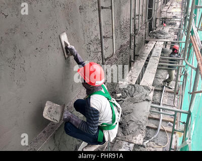 Bauarbeiter verputzarbeiten Wand mit Zementputz auf der Baustelle. Sie sind das Tragen geeigneter Schutzausrüstung, um zu verhindern, dass Schlimmes passieren. Stockfoto