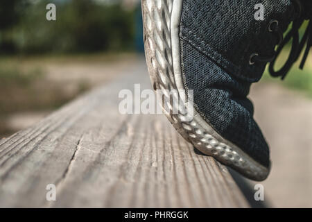 Ein Jugendlicher die Zehenspitzen auf einem hölzernen Schwebebalken bereit zu springen an der Schule Ausbildung Hof an einem Sommertag. Kopieren Sie Platz. Stockfoto