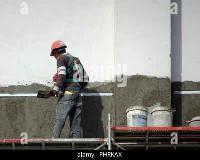 Bauarbeiter verputzarbeiten Wand mit Zementputz auf der Baustelle. Sie sind das Tragen geeigneter Schutzausrüstung schlecht geschehen zu verhindern. Stockfoto