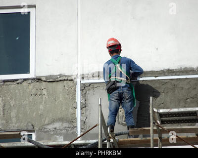 Bauarbeiter verputzarbeiten Wand mit Zementputz auf der Baustelle. Sie sind das Tragen geeigneter Schutzausrüstung schlecht geschehen zu verhindern. Stockfoto