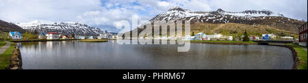 Ein Panoramablick sonnige Aussicht von Seyðisfjörður über dem Wasser und schneebedeckten Gipfeln im Hintergrund begrenzt Stockfoto