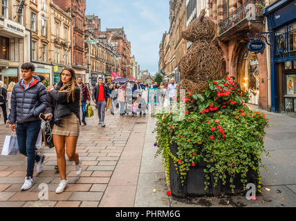 Käufer in der Fußgängerzone der Buchanan Street im Zentrum von Glasgow, Schottland. Ein wicker Teddybär Skulptur auf einem blumenkübel im Vordergrund. Stockfoto