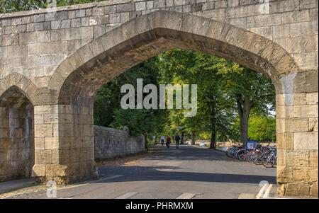 Torbogen neben den Fluss Ouse und Lendal Brücke in York. Menschen flanieren im Schatten neben dem Fluss. Stockfoto