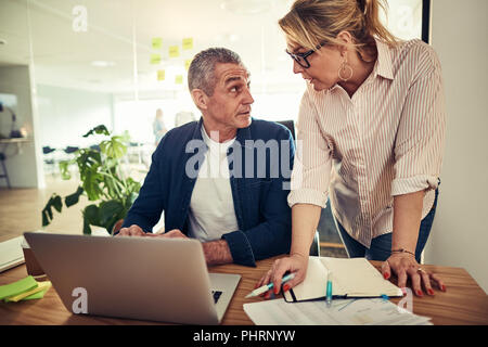 Zwei konzentrierte Reife Kollegen diskutieren gemeinsam über einen Laptop an einem Schreibtisch in einem modernen Büro Stockfoto
