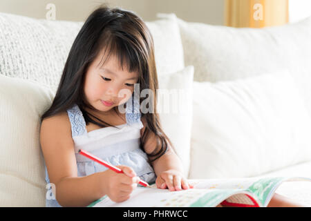 Glücklich süsse kleine Mädchen lächelnd und mit roten Bleistift und Zeichnen, Schreiben auf ein Buch, um Hausaufgaben zu machen. kid Bildung Konzept. Stockfoto