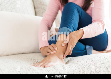 Closeup Frau sitzt auf einem Sofa hält ihre Fußverletzung, Gefühl, Schmerz. Gesundheit und medizinische Konzept. Stockfoto