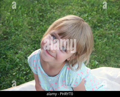 Adorable und glücklichen kleinen Kind Mädchen mit wunderschönen grünen Augen lächeln und der Blick in die Kamera, auf die unscharfen grüne Wiese im Hintergrund Stockfoto