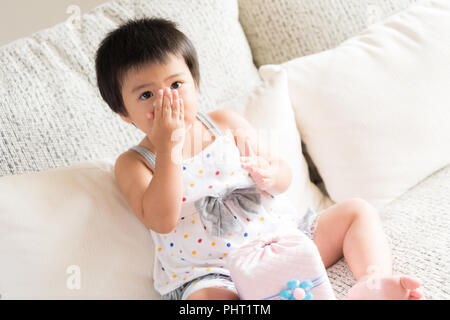 Kranken kleinen asiatischen Mädchen wischen oder Reinigung der Nase mit einem Taschentuch, auf dem Sofa zu Hause sitzen. Medizin und Gesundheit Konzept. Stockfoto