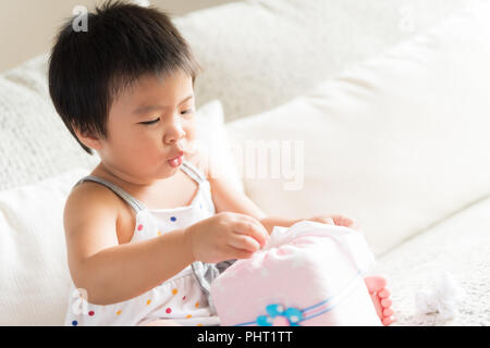 Kranken kleinen asiatischen Mädchen wischen oder Reinigung der Nase mit einem Taschentuch, auf dem Sofa zu Hause sitzen. Medizin und Gesundheit Konzept. Stockfoto