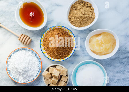 Verschiedene Arten von Zucker und Süßungsmittel in den Schalen, wie Kokos, reine Zuckerrohr, Vereisung, Ahornsirup, Dunkelbraun weiche Zucker, Honig, demerara Cubes Stockfoto