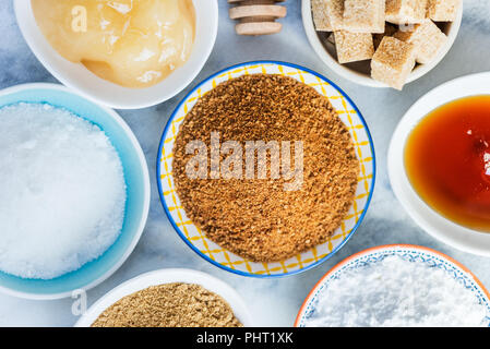 Verschiedene Arten von Zucker und Süßungsmittel in den Schalen, wie Kokos, reine Zuckerrohr, Vereisung, Ahornsirup, Dunkelbraun weiche Zucker, Honig, demerara Cubes Stockfoto