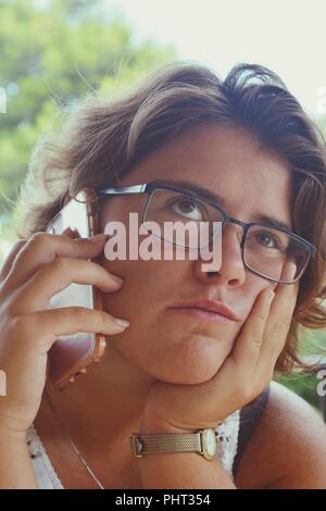 Tausendjährige Frau, mit Handy in der Hand, Hören, mit den Augen und ein gelangweilter/zweifelhafte Ausdruck Stockfoto