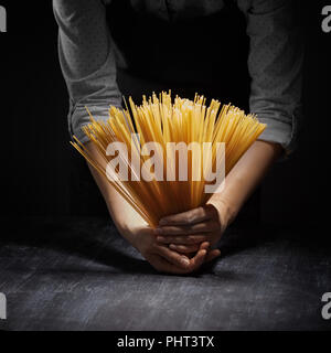 Woman's Hände, die rohe Spaghetti in dunklen Hintergrund Stockfoto