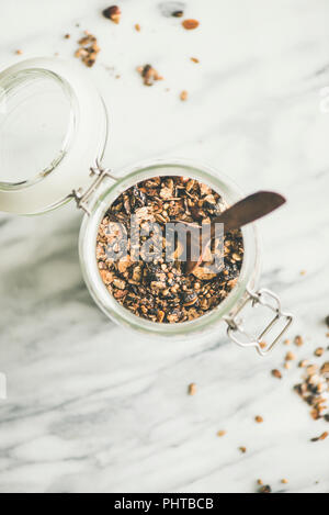 Gesundes Frühstück vorbereitet. Buchweizen und Schokolade Müsli mit Haselnüsse in Glas mit Löffel über hellem Marmor Hintergrund, Ansicht von oben, kopieren. Cl Stockfoto