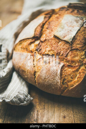 Frisch gebackene Sauerteig Brot aus Weizen Brot über Bettwäsche Serviette und rustikalen Holztisch Hintergrund, selektiver Fokus, vertikalen Zusammensetzung Stockfoto