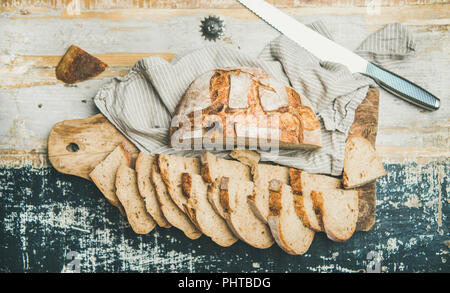 Flachbild-lay von frisch gebackenem Sauerteig Brot aus Weizen Brot halbieren und in Scheiben über Bettwäsche Serviette und rustikalen Holztisch Hintergrund ausschneiden, Ansicht von oben Stockfoto