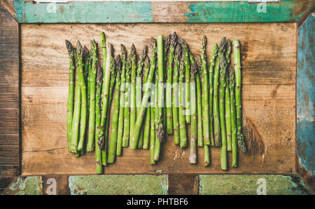 Saisonale Ernte produzieren. Flachbild-lay von Roh ungekocht grüner Spargel in der Zeile über Rustikal fach Hintergrund, Ansicht von oben. Lokaler Markt essen Konzept Stockfoto