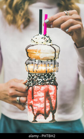 Junge weibliche Holding Sommer kalt Erdbeere Donut freakshake mit Schlagsahne in Mason jar in den Händen, selektiven Fokus Stockfoto