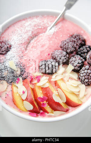 Frischen und kalten strawberry Banana Smoothie garniert mit peach Slices, gefroren Blackberry, Chia Samen und Mandelflocken Stockfoto