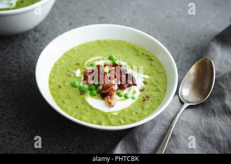 Nahaufnahme von Cremigen grüne Erbsensuppe mit Speck und Kräutern auf grauem Hintergrund Stockfoto